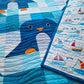 Close up of a penguin on the Chill and Thrill baby quilt showing the navy body, white belly, orange beak and feet, with the nautical sailboat print backing fabric visible alongside