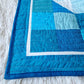 Close up of the corner of the Chill and Thrill penguin baby quilt showing the dark blue binding, white inner border, and scrappy blue patchwork blocks with wave quilting