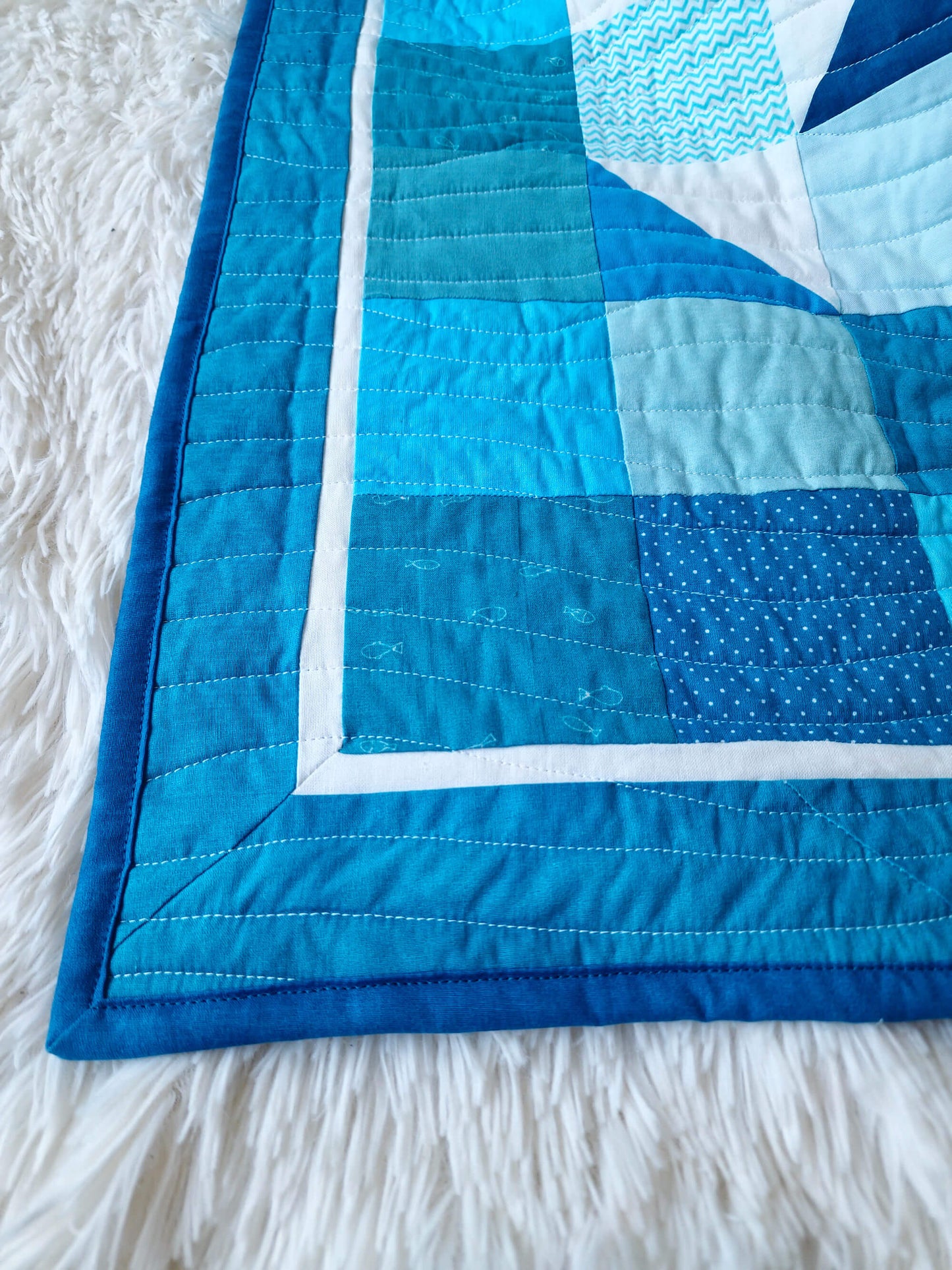Close up of the corner of the Chill and Thrill penguin baby quilt showing the dark blue binding, white inner border, and scrappy blue patchwork blocks with wave quilting
