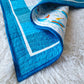 Corner of the Chill and Thrill baby quilt folded back to reveal the nautical sailboat print backing fabric, with dark blue binding and scrappy blue patchwork visible on the front