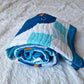 Chill and Thrill baby boy penguin quilt rolled up on a white fluffy surface showing the soft drape and thickness of the quilt with a penguin face and orange beak visible on top