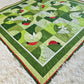 Diagonal view of the Ladybug Wonderland quilt, showing the full design with ladybugs, pinwheel flowers, and vibrant green and red colors.