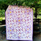 Front view of the 'More than Words' quilt displayed in a serene park setting, with lush green trees in the background, adding a touch of nature to the vibrant quilt design.