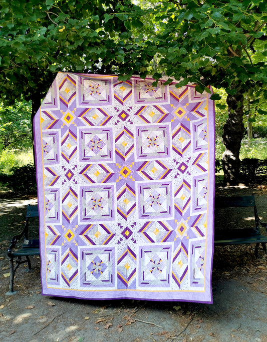 Front view of the 'More than Words' quilt displayed in a serene park setting, with lush green trees in the background, adding a touch of nature to the vibrant quilt design.