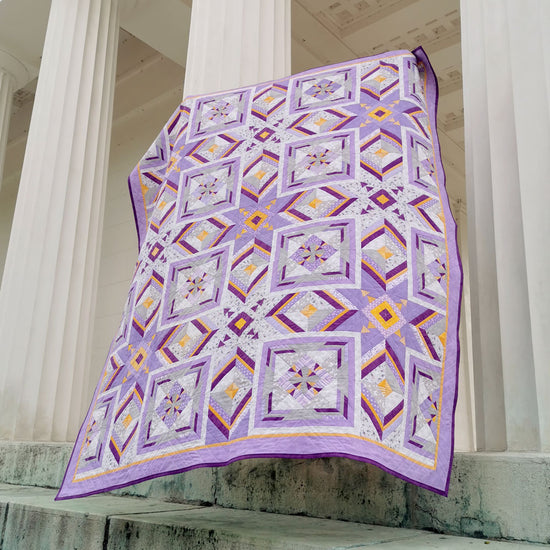 Front view of the 'More than Words' quilt in stunning violet and yellow hues, showcasing the intricate paper piecing design and vibrant color palette.