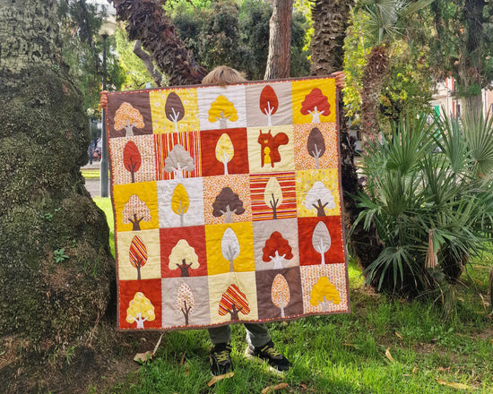 Kid holding a colorful autumn themed Our Forest Autumn quilt with tree patterns in a southern park setting with palm trees