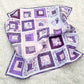 Patchwork quilt with purple and white squares and baby footprints on a light gray background