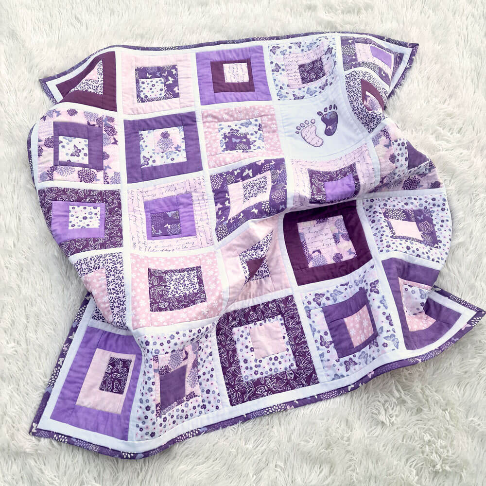 Patchwork quilt with purple and white squares and baby footprints on a light gray background