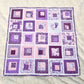 Quilt with purple and pink square patterns and footprint appliques on a white surface