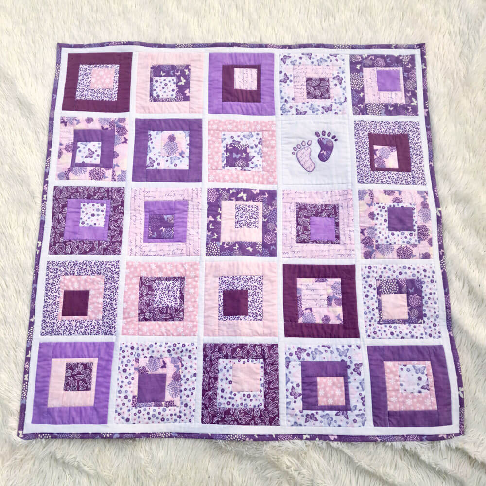 Quilt with purple and pink square patterns and footprint appliques on a white surface